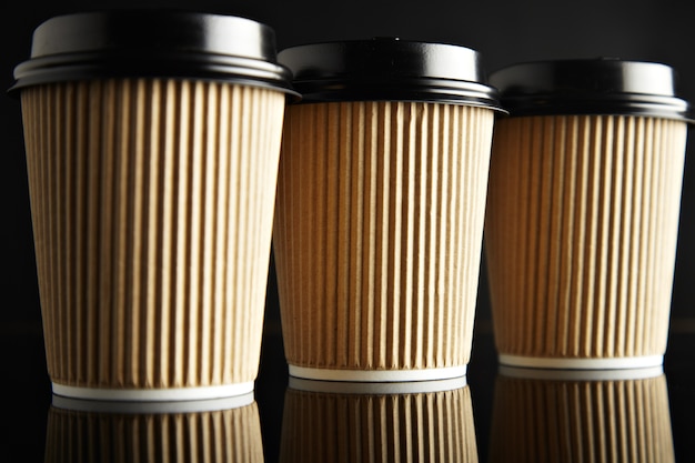 Free photo luxury set of brown take away cardboard paper cups closed with caps isolated on black and mirrored. retail  presentation