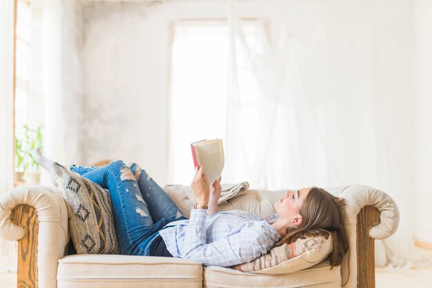 Lying woman reading novel on couch