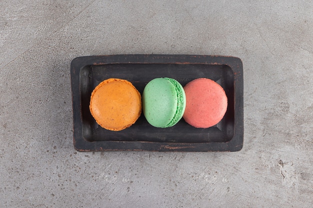 Macaroni cookies of different colors in a dark wooden board.