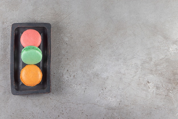 Macaroni cookies of different colors in a dark wooden board . 