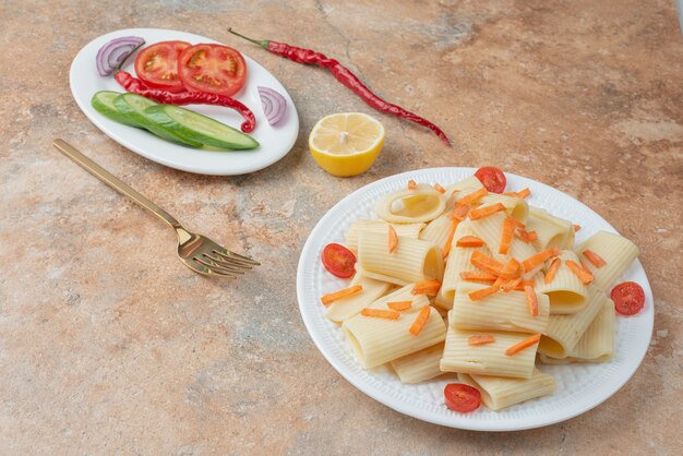 Macaroni with carrot, tomato cherry, cucumber and slice of lemon on white plate