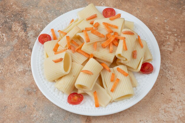 Macaroni with carrot and tomato cherry on white plate.