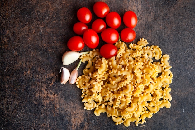 Macaroni with tomatoes and garlic top view on a dark textured background