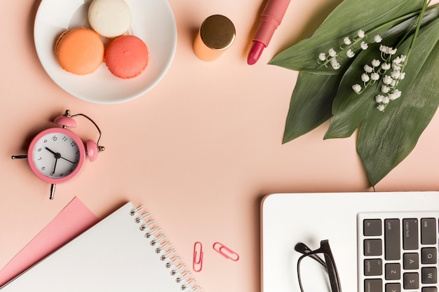 Free Photo macaroons,alarm clock,lipstick,leaves and flower with spiral notepad and laptop