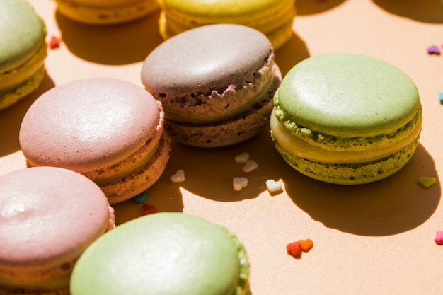 Macaroons with heart shape sprinkles on beige backdrop