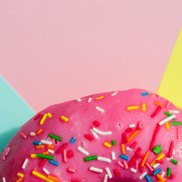 Free photo macro shot of pink donut with colorful sprinkles on colored backdrop