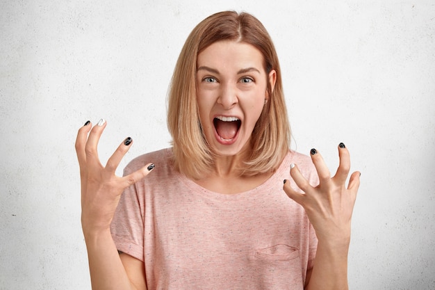 Mad irritated young woman screams loudly and gestures actively, being dissatisfied and annoyed with something, expresses her displeasure and annoyance