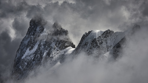 Free photo magical shot of a beautiful snowy mountain peak covered with clouds.