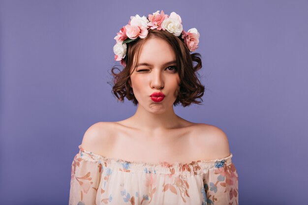 Magnificent white female model with flowers in hair standing. Sensual short-haired girl posing with kissing face expression.