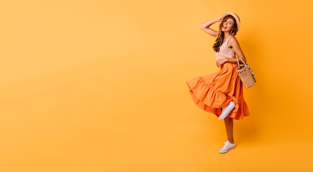 Magnificent woman in long bright skirt dancing in studio. Carefree inspired female model posing with pleasure on yellow.