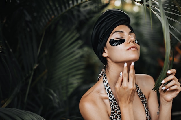 Magnificent woman with eye patches touching chin. European woman in black turban posing on exotic background.