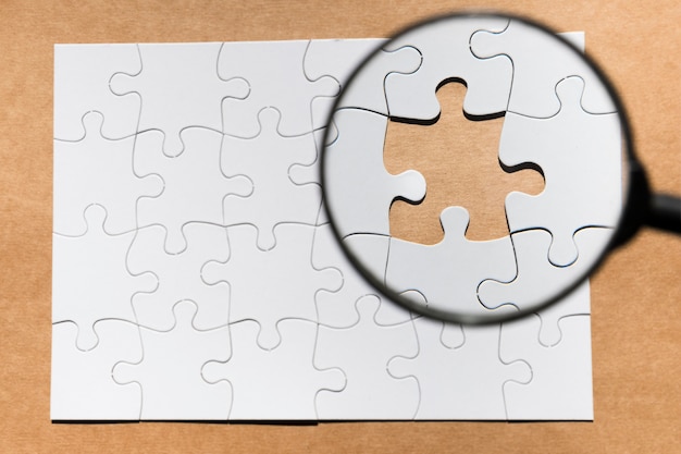 Free Photo magnifying glass on missing puzzle over brown paper textured backdrop