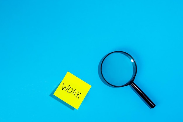 Free photo magnifying loupe and a sticker with the word work on a blue background