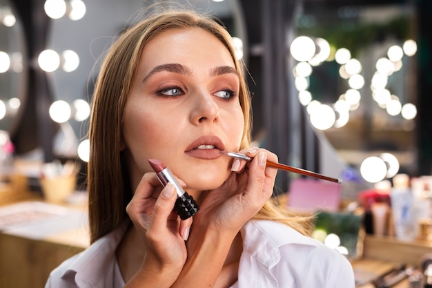 Make-up artist applying lipstick on smiling woman's lips with brush