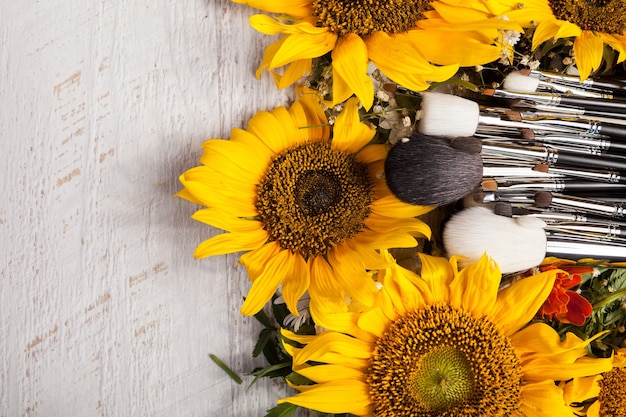 Make up brushes next to beautiful wild flowers on wooden background