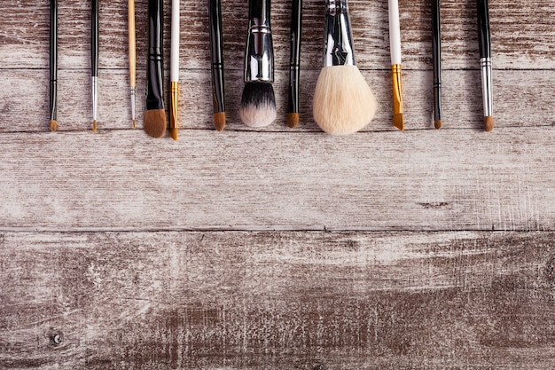 Make up brushes in on top view image on wooden background. Cosmetic products