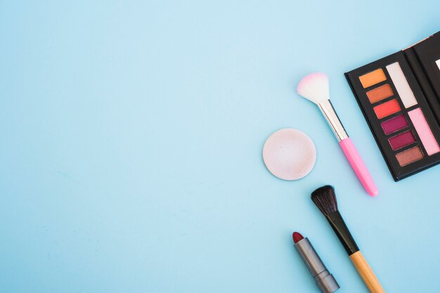 Make-up eyeshadow palette brush; sponge; lipstick on blue background