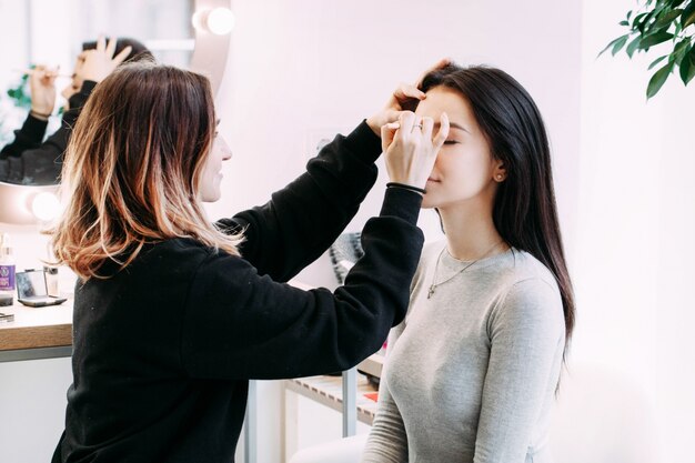 Makeup artist does lady's brows sitting before her