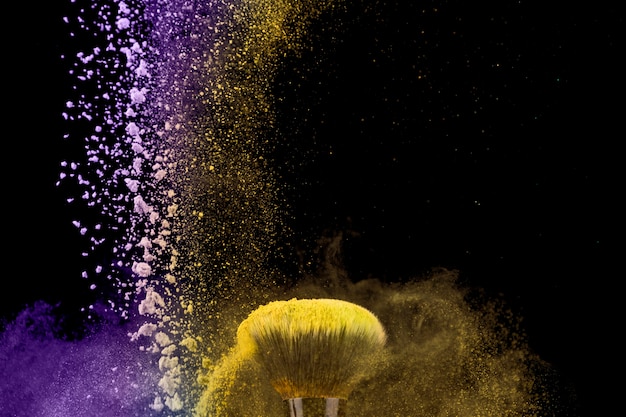 Makeup brush and dust of powder on dark background