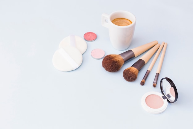 Free photo makeup brush with sponge; eyeshadow and blusher with coffee mug on white background