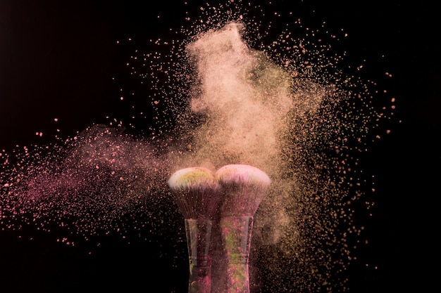 Makeup brushes in burst of beige powder on dark background