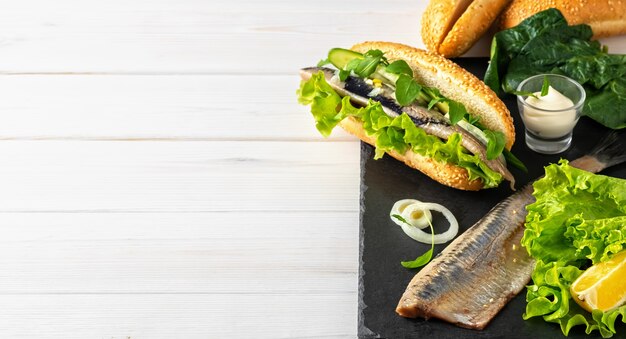 Making a sandwich of herring fillet with onions, cucumber and salad on a stone board