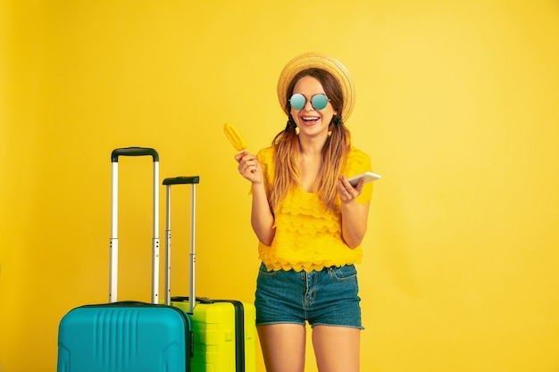 Making selfie before traveling. Caucasian woman's portrait on yellow studio background. Beautiful model in cap. Concept of human emotions, facial expression, sales, ad. Summertime, travel, resort.