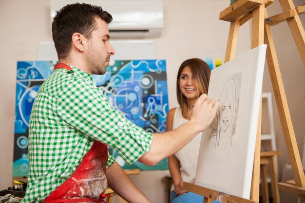 Male artist drawing a sketch of a beautiful young woman in his studio