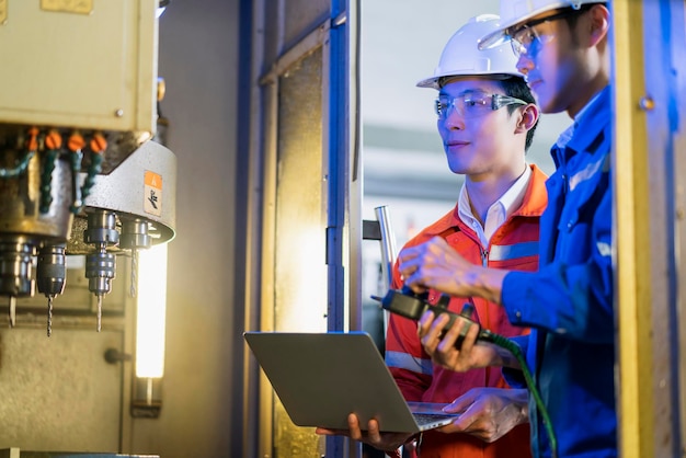 Male Asian engineer professional having a discussion standing concult cnc machine in the factory two asian coworker brainstorm explaining and solves the process of the cnc operate machine