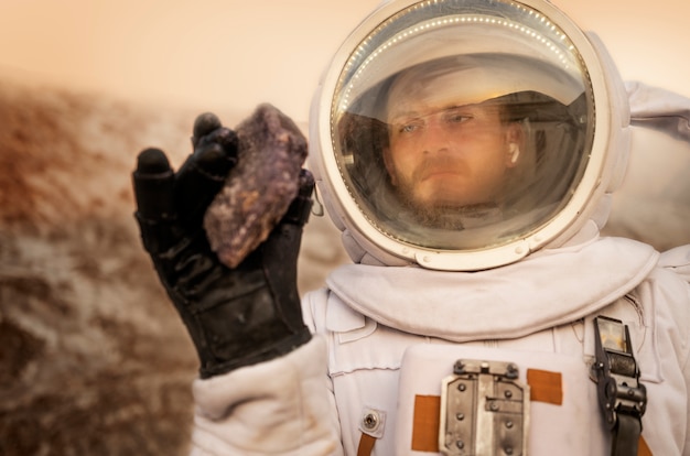 Free Photo male astronaut analyzing a rock during a space mission on another planet