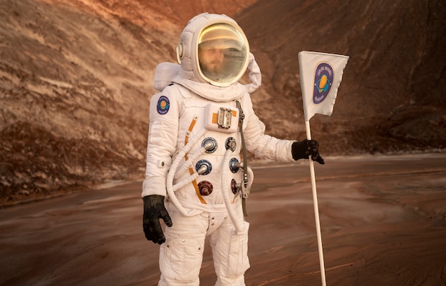 Male astronaut holding a flag stuck in soil on an unknown planet