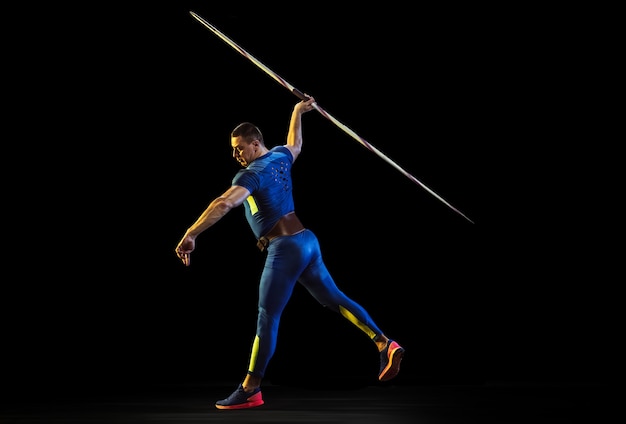 Free photo male athlete practicing in throwing javelin isolated on black studio in neon light