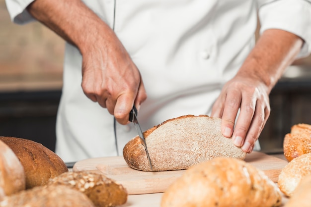 Male baker cutting loaf of bread on chopping bread