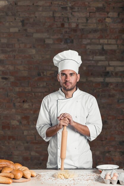 Free photo male baker standing behind the table with dough; ingredients; and baked bread