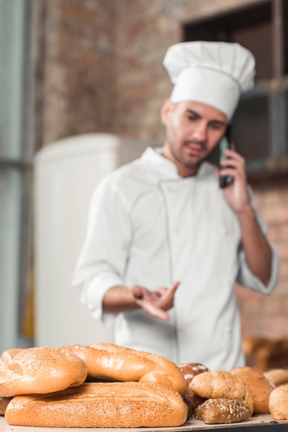 Free photo male baker talking on cellphone behind the loaf of breads