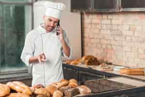 Free photo male baker talking on cellphone standing in bakery gesturing