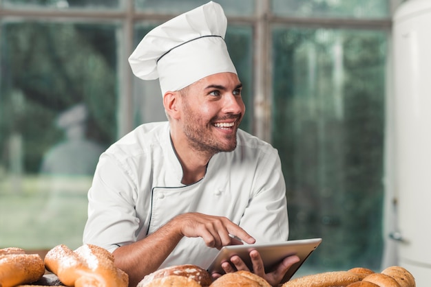 Male baker using digital tablet with baked breads