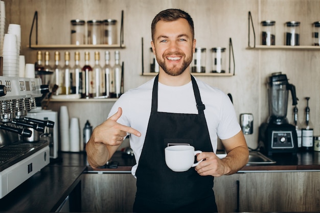 Free photo male barista at coffee shop holding cup by the counter