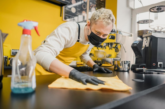 Male barista with medical mask cleaning table