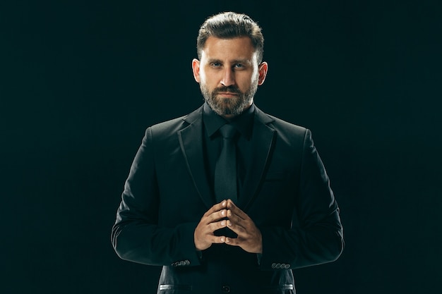 Male beauty concept. Portrait of a fashionable young man with stylish haircut wearing trendy suit posing over black studio background.