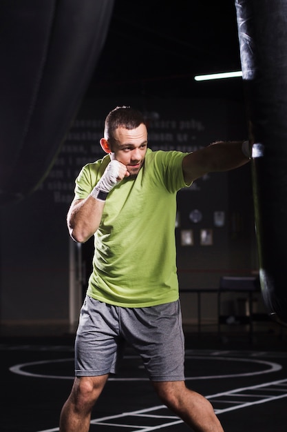 Male boxer wearing t-shirt and shorts practicing with punching bag