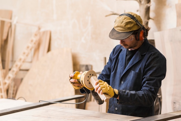 A male carpenter working with orbital sander for shaping wooden block