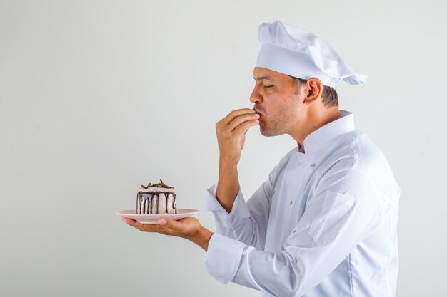 Male chef cook holding cake and making tasty gesture in hat and uniform