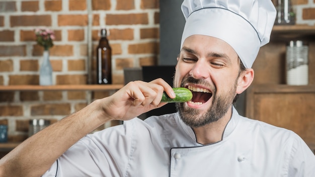 Free photo male chef eating fresh cucumber in the kitchen