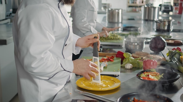 Free Photo male chef grating parmesan cheese on kitchen grater to cook gastronomy recipe in professional cuisine. authentic cook preparing shredded cheddar ingredient to make gourmet meal dish.