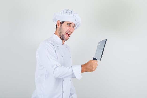 Male chef holding cleaver in white uniform and looking aggressive.