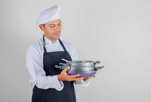 Male chef holding pans with wooden utensils in hat, apron and uniform