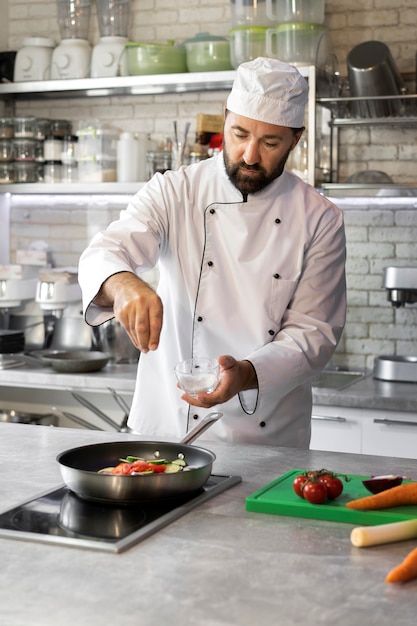 Free photo male chef in the kitchen cooking dish in a frying pan