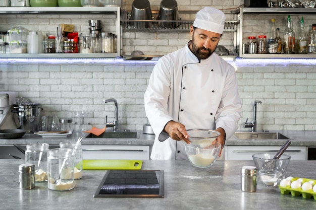 Free photo male chef in the kitchen sifting flour