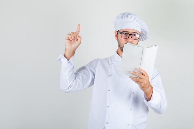 Male chef reading book and doing finger up in white uniform